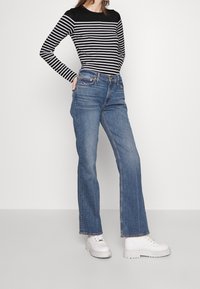 Chemise à rayures noires et blanches à manches longues associée à un jean droit bleu et des chaussures à plateforme blanches. Design simple avec des accents minimaux.
