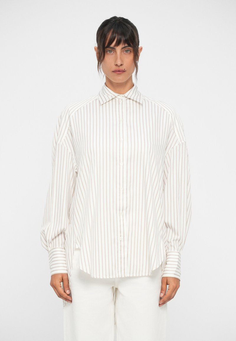 Camisa branca com riscas verticais bejas subtis, apresentando um colarinho clássico, mangas longas e um corte solto, feita de um tecido leve.