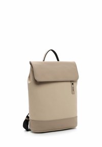 Zaino in pelle beige con un ribaltabile, manico superiore, spallacci neri regolabili e un sottile etichetta con logo sul lato.