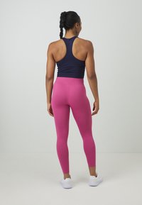 Débardeur bleu marine à dos nageur, associé à des leggings roses taille haute. Tissu lisse, design ajusté, et chaussures de sport blanches.