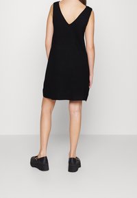 Robe noire sans manches avec un dos en V, fabriquée en tissu doux, reposant au-dessus des genoux. Associée à des chaussures à plateforme noires.
