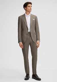 Szary garnitur w kratę z dopasowanymi spodniami, biała koszula i czarne skórzane buty; dopasowany krój z klapami z wycięciem i ozdobną poszetką.