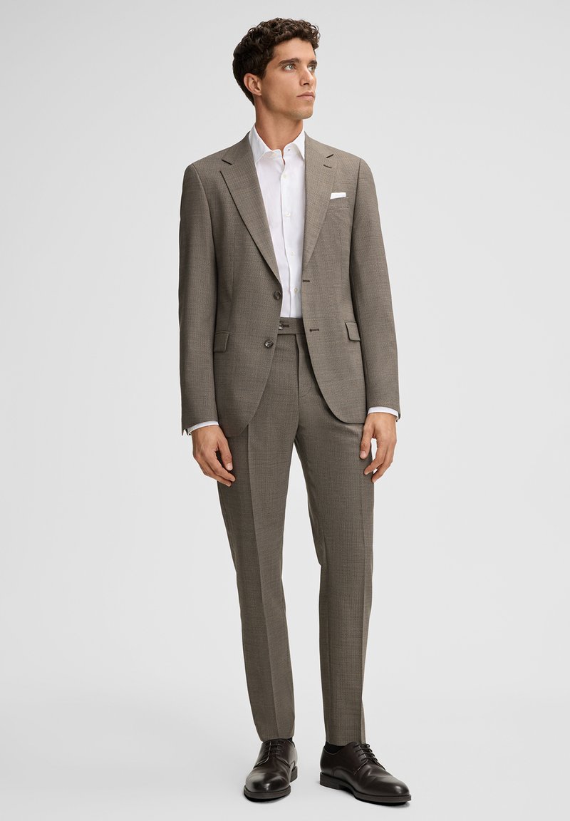 Szary garnitur w kratę z dopasowanymi spodniami, biała koszula i czarne skórzane buty; dopasowany krój z klapami z wycięciem i ozdobną poszetką.