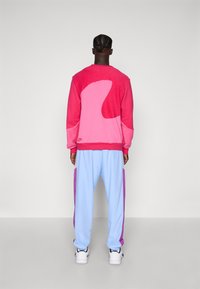Lyserød og lyseblå træningsdragt med et stort abstrakt lyserødt design på bagsiden af sweatshirt'en og lilla detaljer på bukserne.