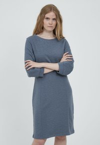 Siva teksturirana haljina s rukavima do tri četvrtine i okruglim izrezom. Tkanina ima suptilan uzorak i prilagođen kroj.