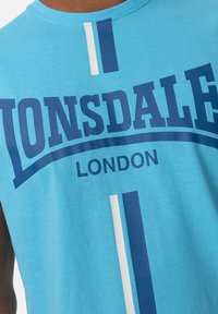 Gaiši zils kokvilnas topiņš, kas raksturīgs ar lieliem tumši ziliem uzrakstiem "Lonsdale" un "London", kā arī vertikālām baltām un tumši zilām svītrām. Mīksta tekstūra.