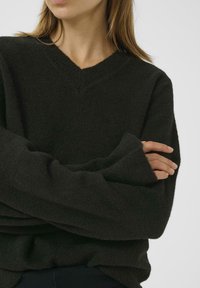 Black, textured knit sweater with a V-neck and loose sleeves, showcasing a cozy, relaxed fit design. No visible patterns or hardware.