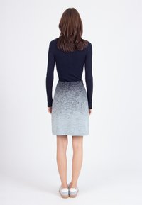 Marineblauw geribbeld langemouwtop gecombineerd met een knielange grijze ombre rok met een textuurpatroon, afgewerkt met schoenen met een witte zool.