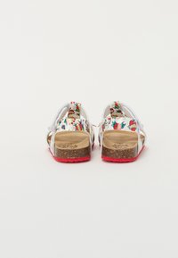 White sandals with floral patterns, cork midsole, and red rubber outsole; secured with adjustable straps for a comfortable fit.
