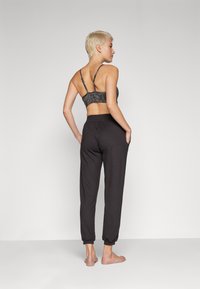 Fekete rugalmas jogging nadrág gumis szegéllyel és egy egyszínű fekete mintás bralette-tel. A modell hátulról látható, kezével a zsebekben.