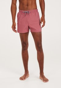 Plavecké šortky v púdrovej ružovej farbe, vyrobené z ľahkej tkaniny. Majú elastický pás so šnúrkou a bočné vrecká.