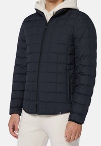 Marinblå uppblåst jacka med ett kviltat mönster, dragkedjestängning och sidofickor. Tyget har en slät yta och inkluderar en huva.