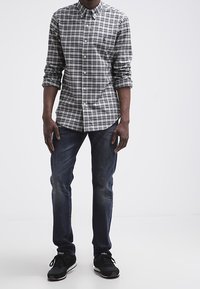 Camisa de cuadros negra y gris con botones y mangas largas, combinada con jeans oscuros y zapatillas negras con acentos blancos.