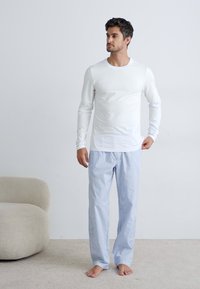 Langermet hvit topp og blåstripete pysjamasbukser. Stoffet ser glatt ut, og buksene har strikk i livet. Ingen fottøy.
