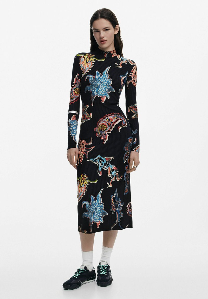 Vestito midi nero a coste con motivi astratti colorati, maniche lunghe e scollatura alta, abbinato a sneakers nere e calze bianche.