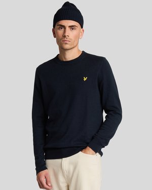 Navy blue knit sweater with a ribbed crew neck and cuffs, featuring a small yellow logo accent on the chest. Worn with light-colored pants.