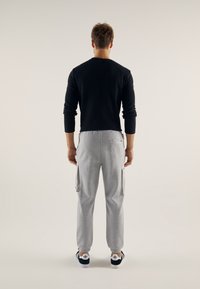 Černé žebrované tričko s dlouhými rukávy a šedé tepláky s cargo kapsami, které mají volný střih a zužující se manžety, nošené s tmavě modrými teniskami.