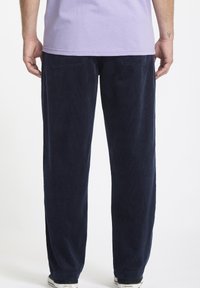 Pantalons en velours côtelé bleu marine à coupe droite, avec poches arrière et texture subtilement côtelée, associés à un t-shirt lavande.