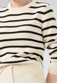 Sweter dzianinowy z poziomymi czarnymi paskami na kremowym tle. Okrągły dekolt, prążkowany dół i mankiety. Teksturowana tkanina.