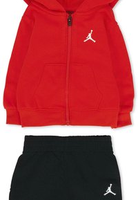 Rode zip-up hoodie met voorkwabben en wit Jordan-logo; gecombineerd met zwarte sweatpants met elastische taille en witte logo-accent. 