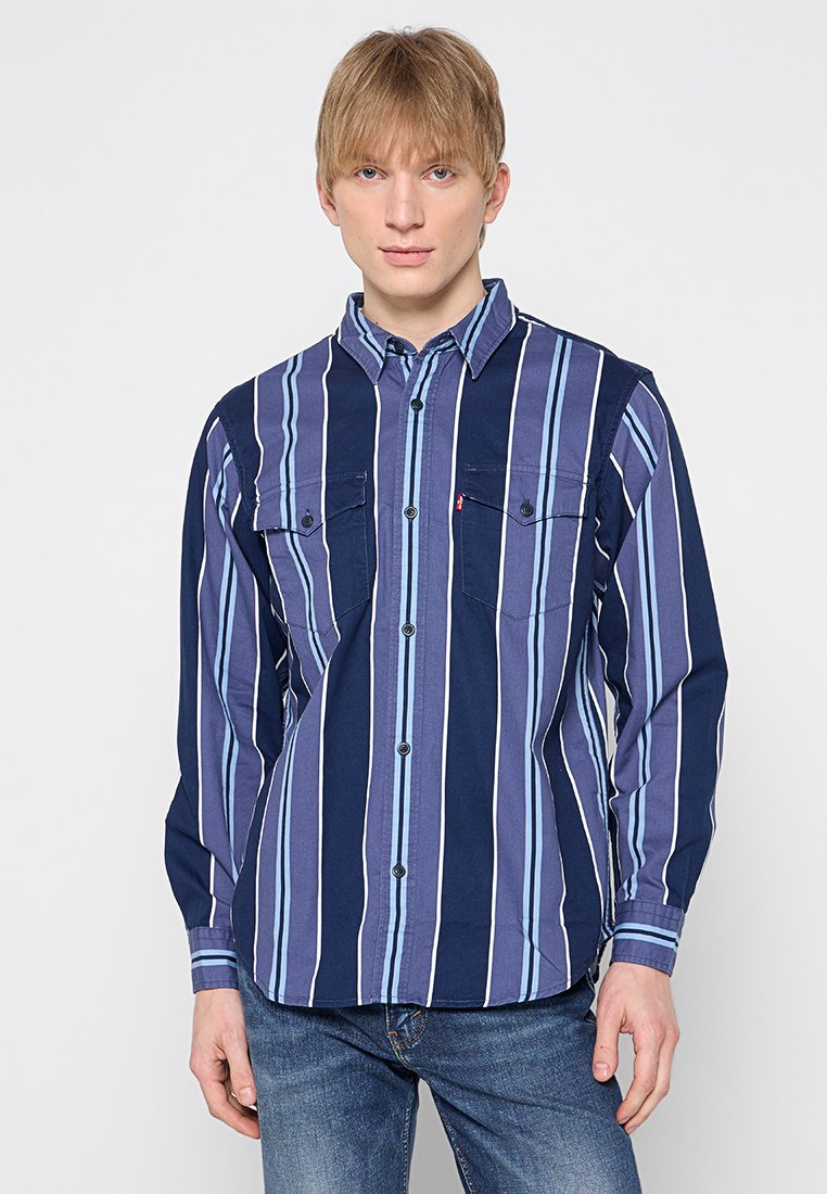 Maglietta a maniche lunghe di colore blu navy con strisce verticali azzurre e bianche. Presenta colletto con bottoni e due tasche sul petto. Tessuto di cotone.