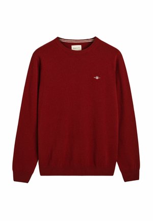 Jersey de punto rojo con cuello redondo, puños y bajo acanalados. Presenta un pequeño logo bordado en el lado izquierdo del pecho. Textura suave.