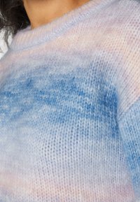 Pull en maille dans des couleurs pastel douces et mélangées de bleu et rose, avec une coupe ample et un col rond côtelé. La texture est duveteuse et légère.