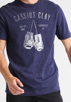 T-shirt bleu marine avec un motif blanc de gants de boxe vintage, texte « Cassius Clay », « 22 juillet 1981 » et « Louisville KY » sur le devant.