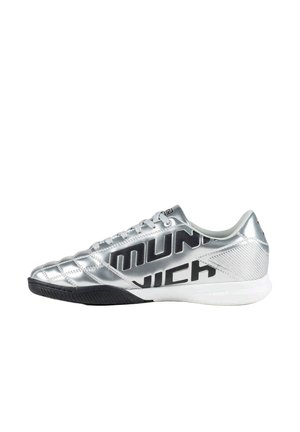 Zapatilla de fútbol sala plateada con suela negra y gran texto negro ""MUNICH"" en el lateral, vista desde el lado exterior.
