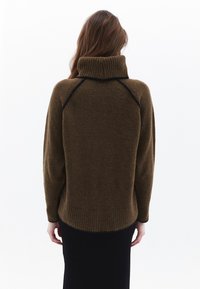Bruine oversized trui met een geribde col, raglanmouwen en zwarte rand langs de schouders. Zachte, gestructureerde stof.