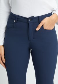 Navy blue stretch pants with a smooth texture, featuring a zip and button closure, two front pockets, and visible stitching details.