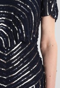 Gros plan sur une robe bleu foncé avec des rayures diagonales en sequins argentés et une manche courte sur un bras nu.
