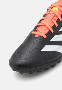 Zwarte voetbalschoen met een gestructureerde bovenkant, oranje veters en witte streepaccenten. Heeft een gemodelleerde zool voor grip op verschillende oppervlakken.