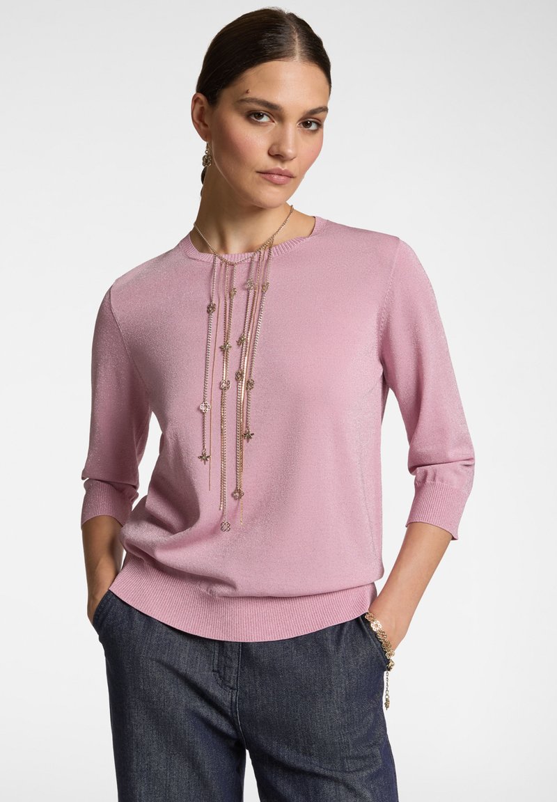 Maglione rosa a maglia con maniche a tre quarti, orlo a coste e collana decorativa lunga con accenti metallici e forme floreali.