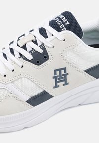 Zapatillas blancas y marinas que combinan materiales de ante y malla, con un cuerpo texturizado, acentos oscuros contrastantes y detalle de marca en la lengüeta.