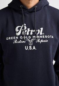 Námořnická modrá mikina z bavlněné směsi, s grafickým logem na přední straně v bílé barvě, s kapucí na šňůrku a měkkým, texturovaným povrchem.