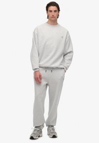 Light gray sweatshirt with ribbed cuffs and logo detail, paired with matching gray sweatpants featuring an elastic waistband and side pockets.
