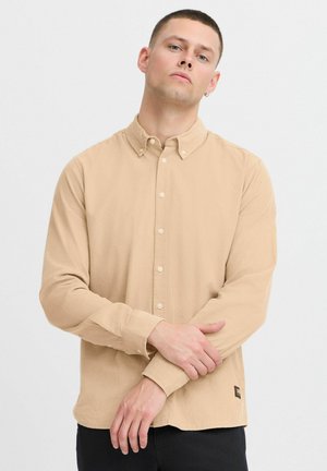 Beige knappskjorte med teksturert overflate, lange ermer og krage. Har små knapper og et merke på sømmen.