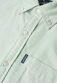 Camicia verde chiaro a bottoni realizzata in tessuto testurizzato, con bottoni bianchi e una tasca con etichetta blu "Superdry".