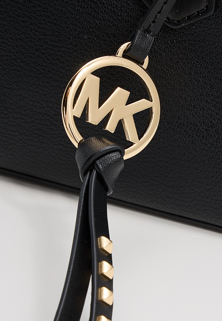 Sac en cuir noir avec texture grainée, présentant un accent logo circulaire doré. Une bandoulière ornée de clous pyramides dorés ajoute du détail au design.