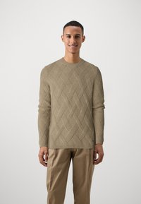 Pulover bej tricotat cu un model țesut, guler rotund și mâneci lungi, asociat cu pantaloni bej. Textură netedă, croi lejer.