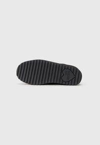 Suela de zapato negra con ranuras horizontales y un logo en forma de corazón que dice "LOVE MOSCHINO" cerca del tacón sobre un fondo blanco.