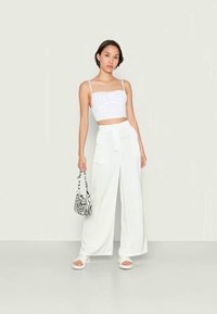 Top branco cropped com alças finas e um padrão texturizado, combinado com calças largas brancas. Os acessórios incluem uma mala com padrão de zebra em preto e branco.