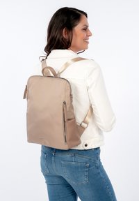 Zaino in nylon beige con design strutturato, tasca anteriore con zip e spalline regolabili a contrasto. Texture liscia, accenti minimalisti.