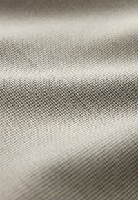 Gros plan sur un tissu beige clair avec un petit motif de tissage texturé et de doux plis créant des ombres douces.
