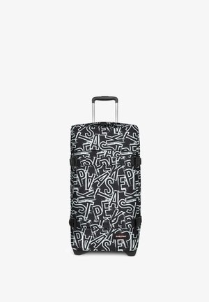Valise rigide noire et blanche avec un motif abstrait de logo Eastpak, poignée télescopique et deux sangles latérales réglables.