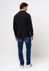 Svart langermet polo skjorte med rett kant og ribbet krage, kombinert med slim-fit blå jeans og hvite sneakers med røde detaljer.