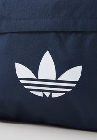 Laikku sininen kangaskassi, jossa on valkoinen trefoili-logo, jossa on kolme lehteä ja kolme vaakasuoraa raitaa alaosassa. Rakenne materiaali.