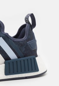 Tmavě modrá teniska s texturovaným síťovaným svrškem, světle modrými pruhy, gumovou patní částí a bílou mezipodešví s žebrovaným designem.