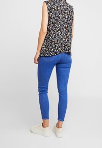 Blommig ärmlös topp i svart med gula och vita mönster, ihopparad med blå skinny jeans och ljusa sneakers med tjock sula.